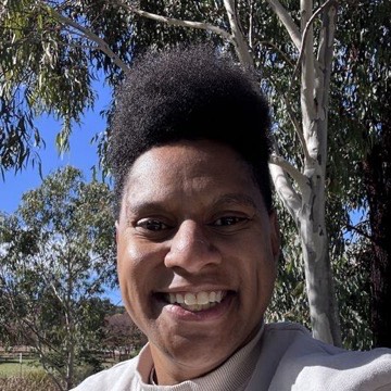 Nikki Monks smiling, standing under a gum tree in Canberra.